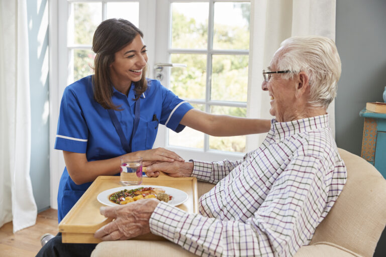 Nurse serving dinner to a senior man in an armchair at home
