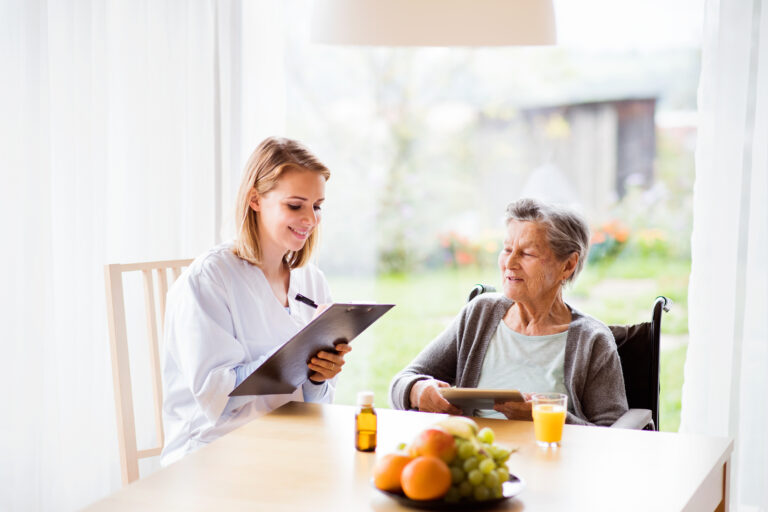 Health visitor and a senior woman with tablet during home visit. A nurse making notes.